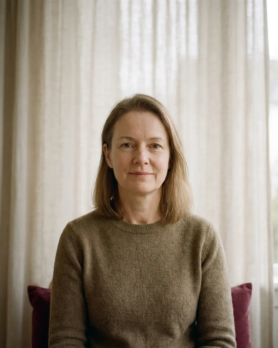 A woman with shoulder-length hair that is thinning at the part, seated in a consultation room.