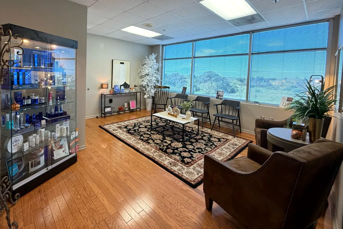 The waiting room at Precision Medical Aesthetics in Bryan, with a wall of windows looking out over the trees.